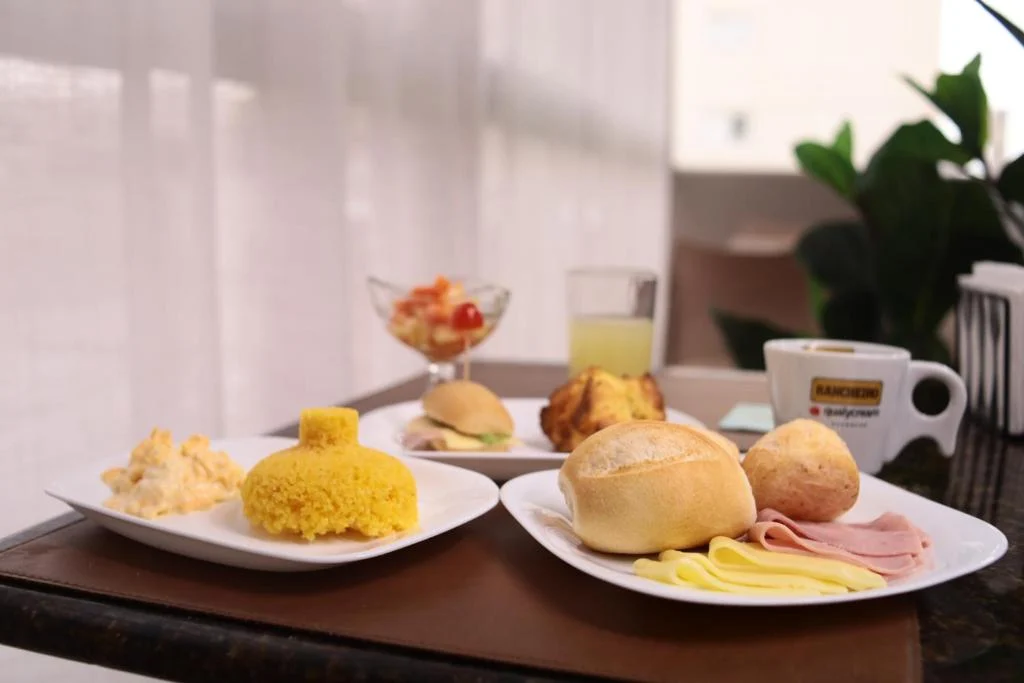 Pratos do café da manhã do House Inn Hotel com pães, frios, suco e café