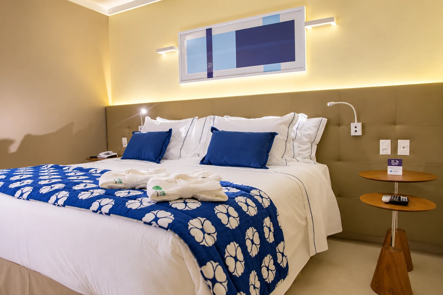 Suíte do House Inn Hotel com cama de casal, peseira azul e iluminação aconchegante